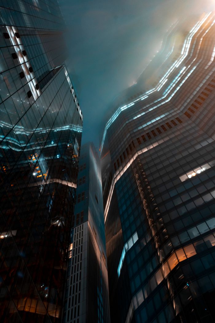 A dramatic low-angle view of illuminated skyscrapers at night in an urban setting.